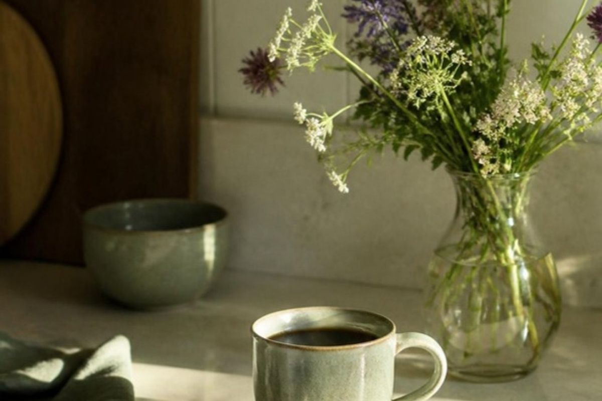 A mug of coffee beside a jar of wildflowers in morning light