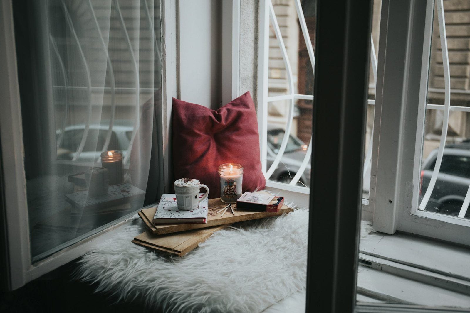 A cozy window seat with a candle, pillow and books